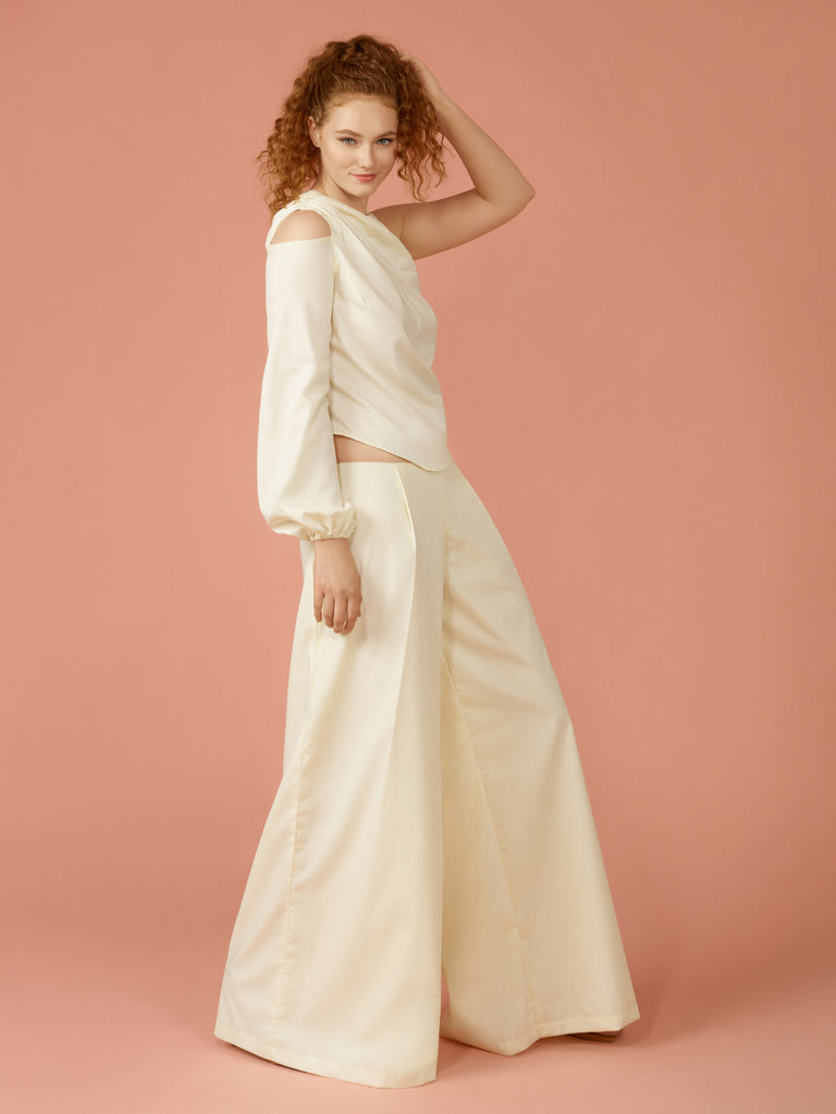 Side view of off white draped asymmetric blouse and matching off white wide leg trouser